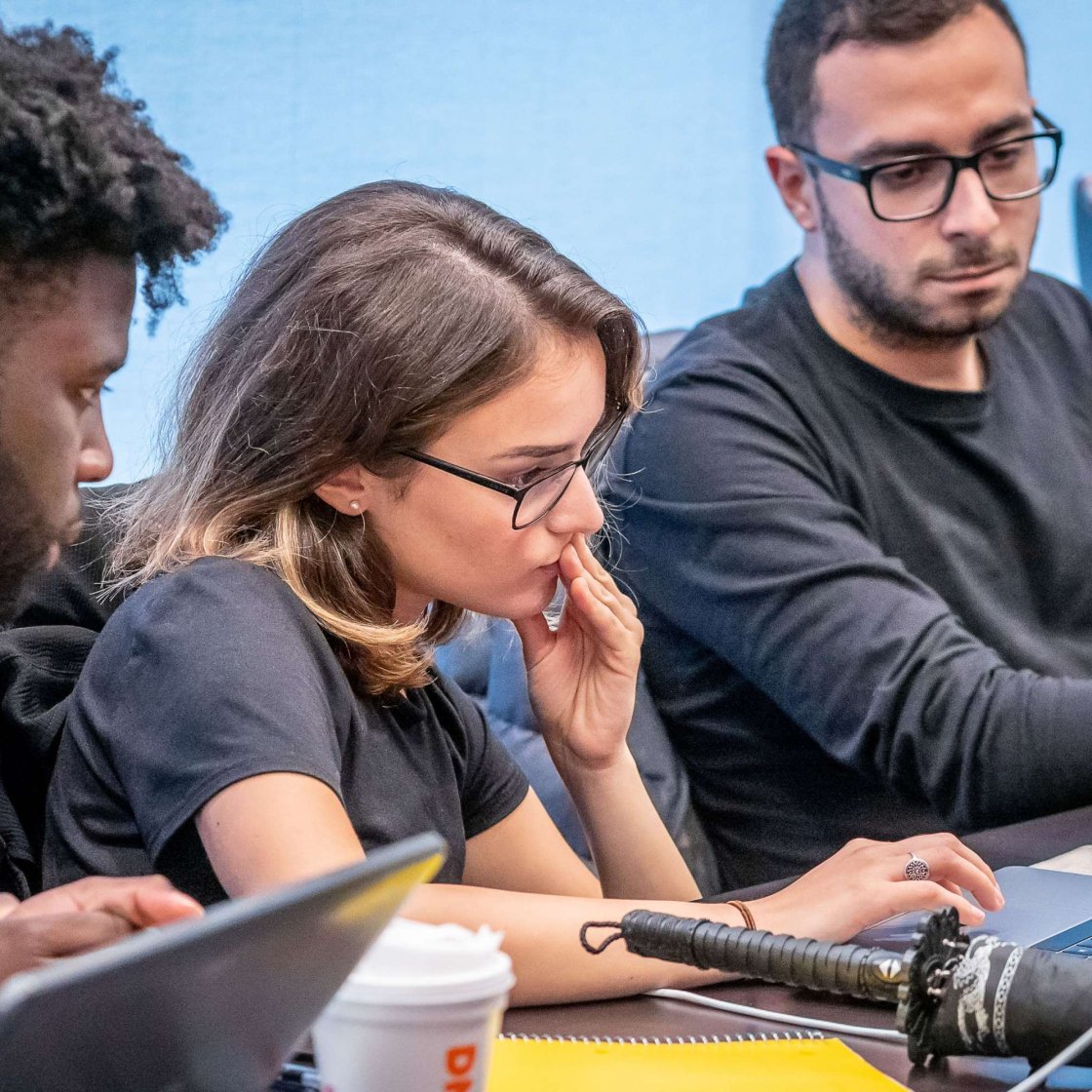 Three students huddled around a laptop examining data recorded from a large microphone next to the laptop.