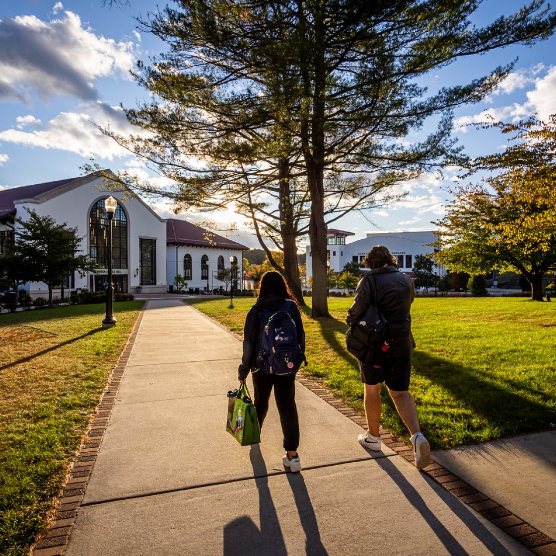 Two students walking together on campus as the sun is beginning to set.