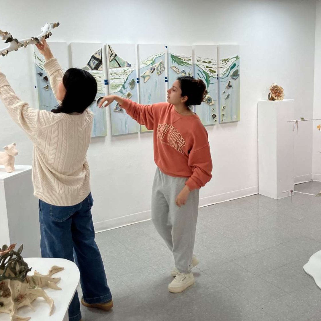 Two students in a gallery, one student holding a sculpture up.