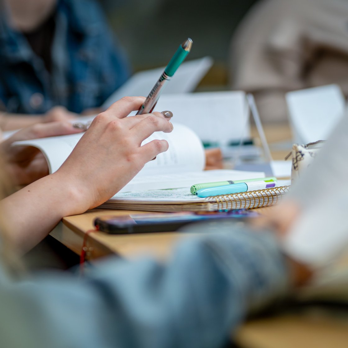 Close-up of a student’s hand holding a pen over an open notebook at a desk.