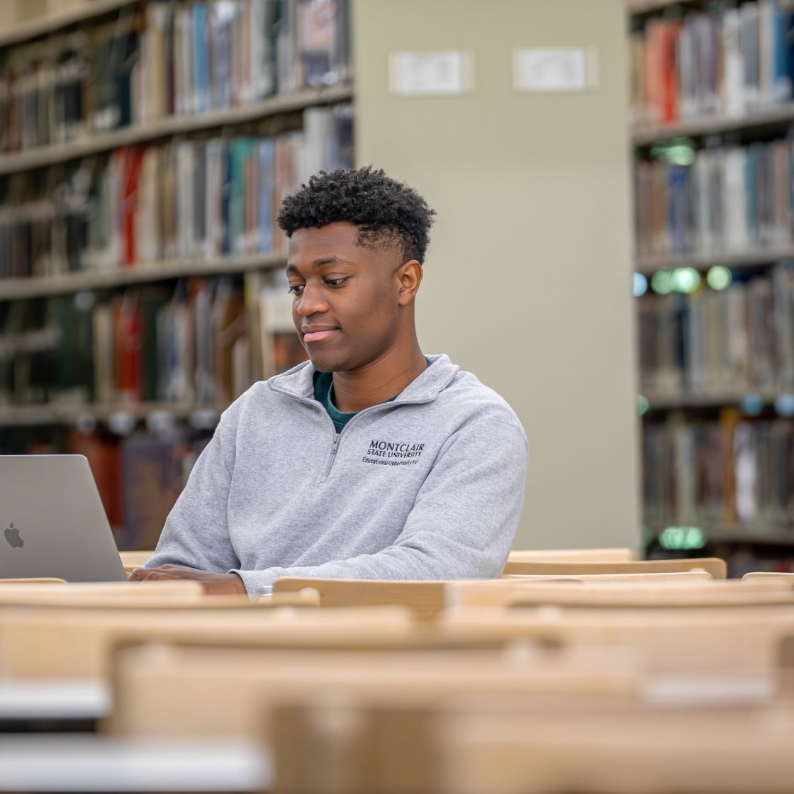 Student sits at a desk in a library setting while working on a laptop computer.