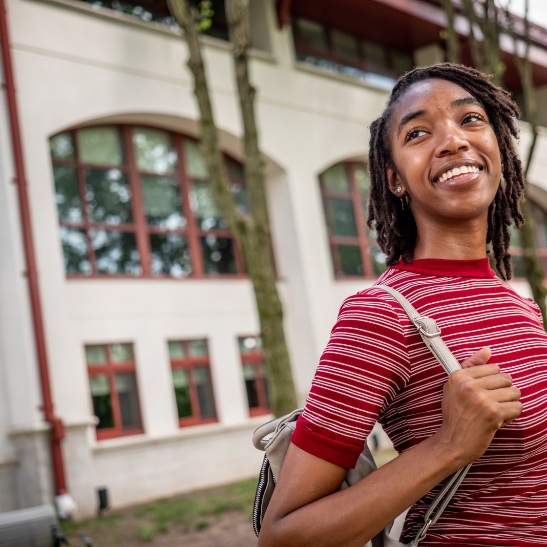 Student with a backpack on her side is smiling.