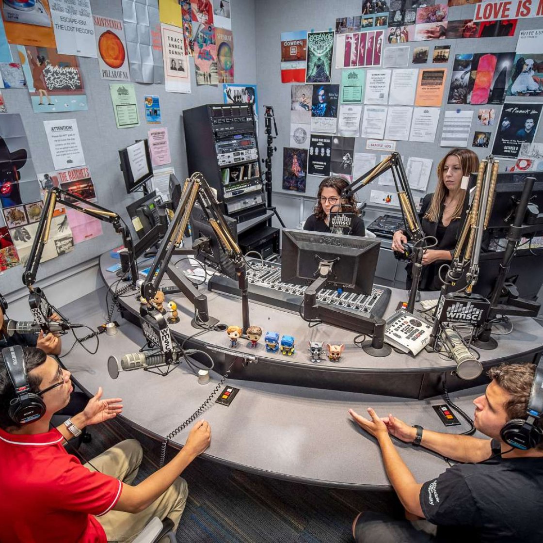 overhead view of students seated at a round table with headphones and microphones in Montclair's radio studio