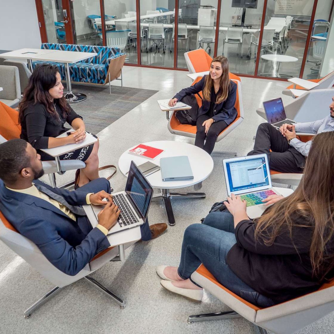 Five students in conversation, sitting in lounge chairs arranged in a circle.