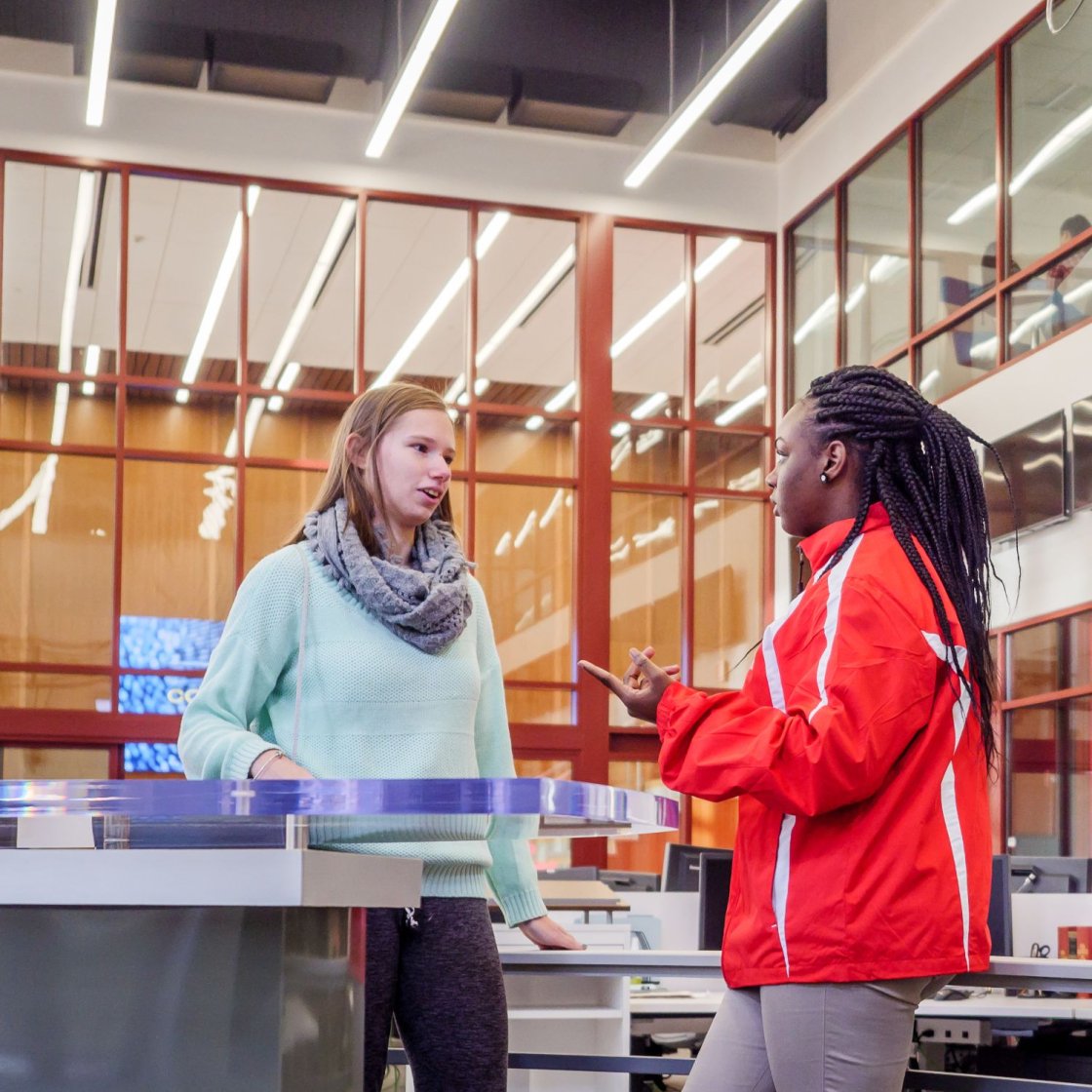 Two students are conversing while standing.