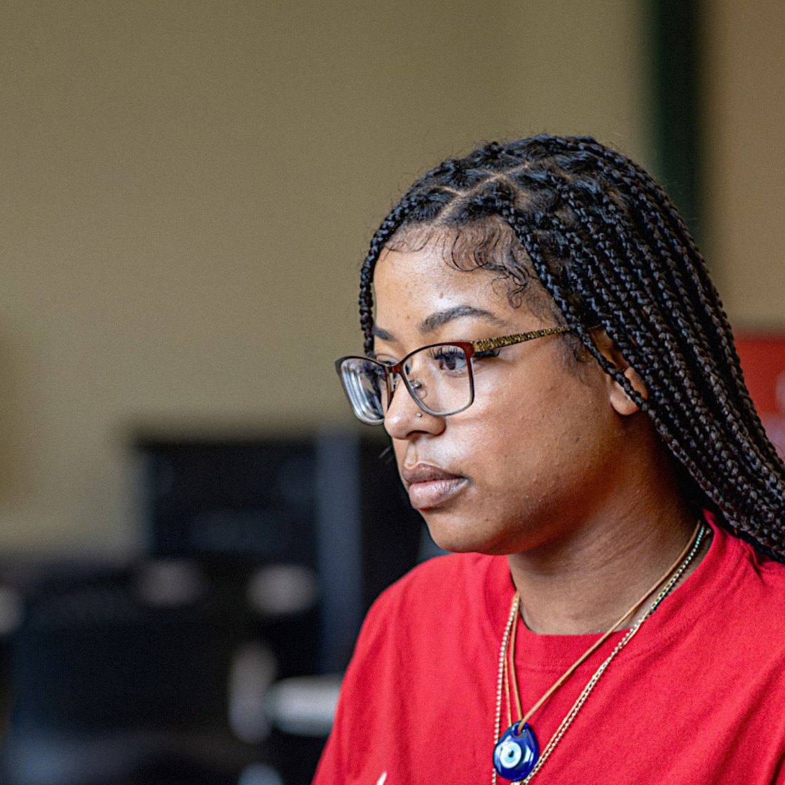 Female student wearing a Bloomfield College shirt is seen typing on a laptop focused on her task.