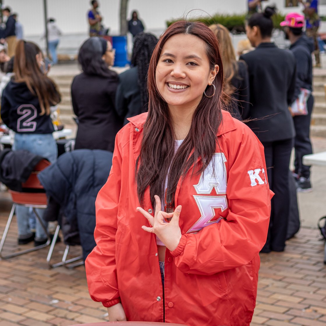 Female student using her Greek sign with a red jacket on.