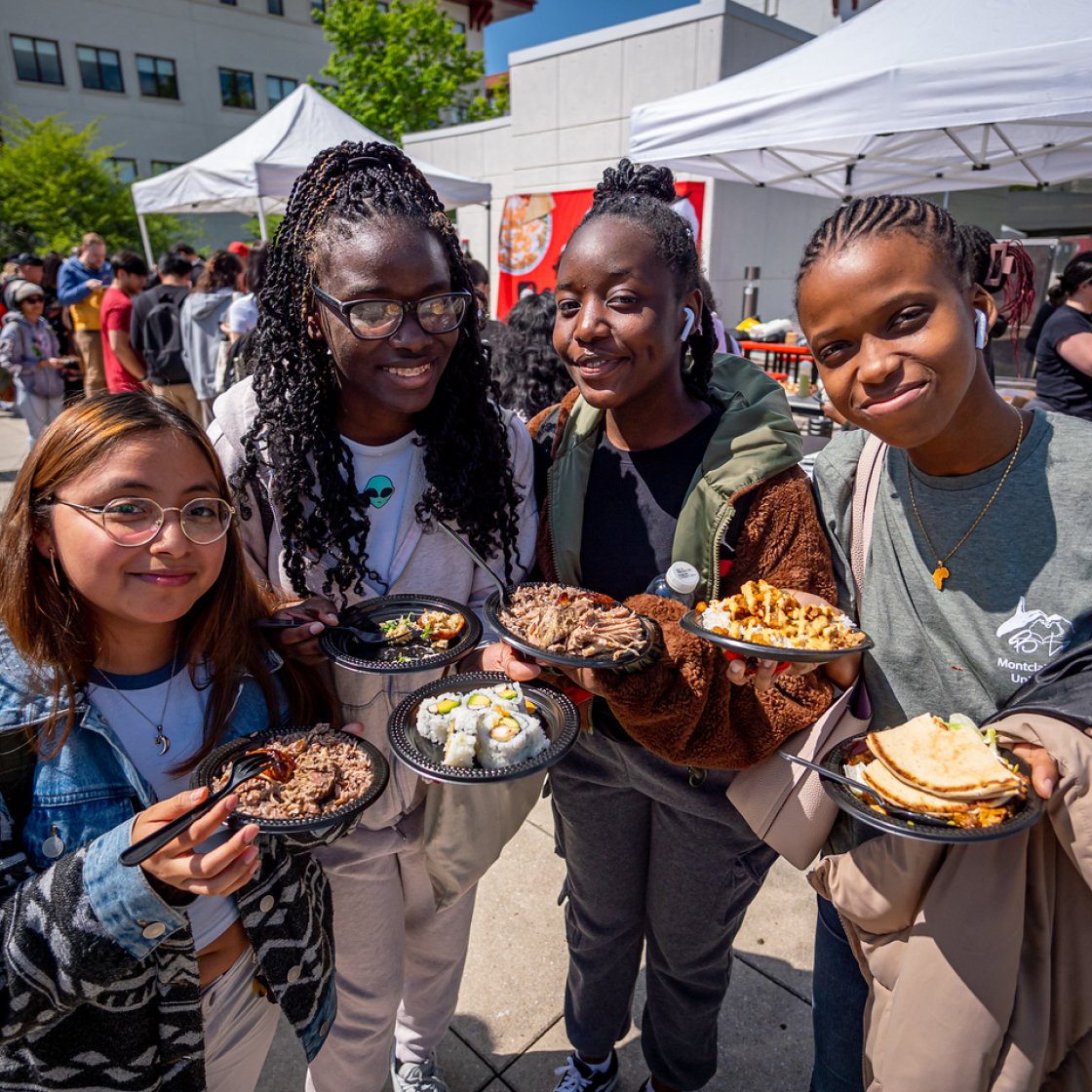 Students holding up various plates of food, smiling.