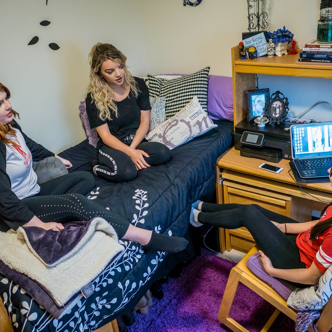 Three female students are together in a dorm room. 