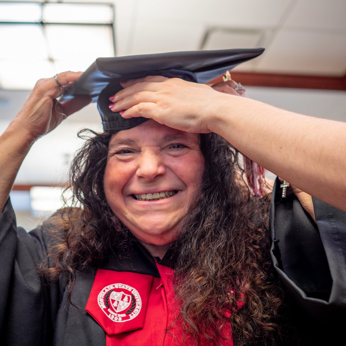 Graduate in cap and gown adjusts their mortarboard. 