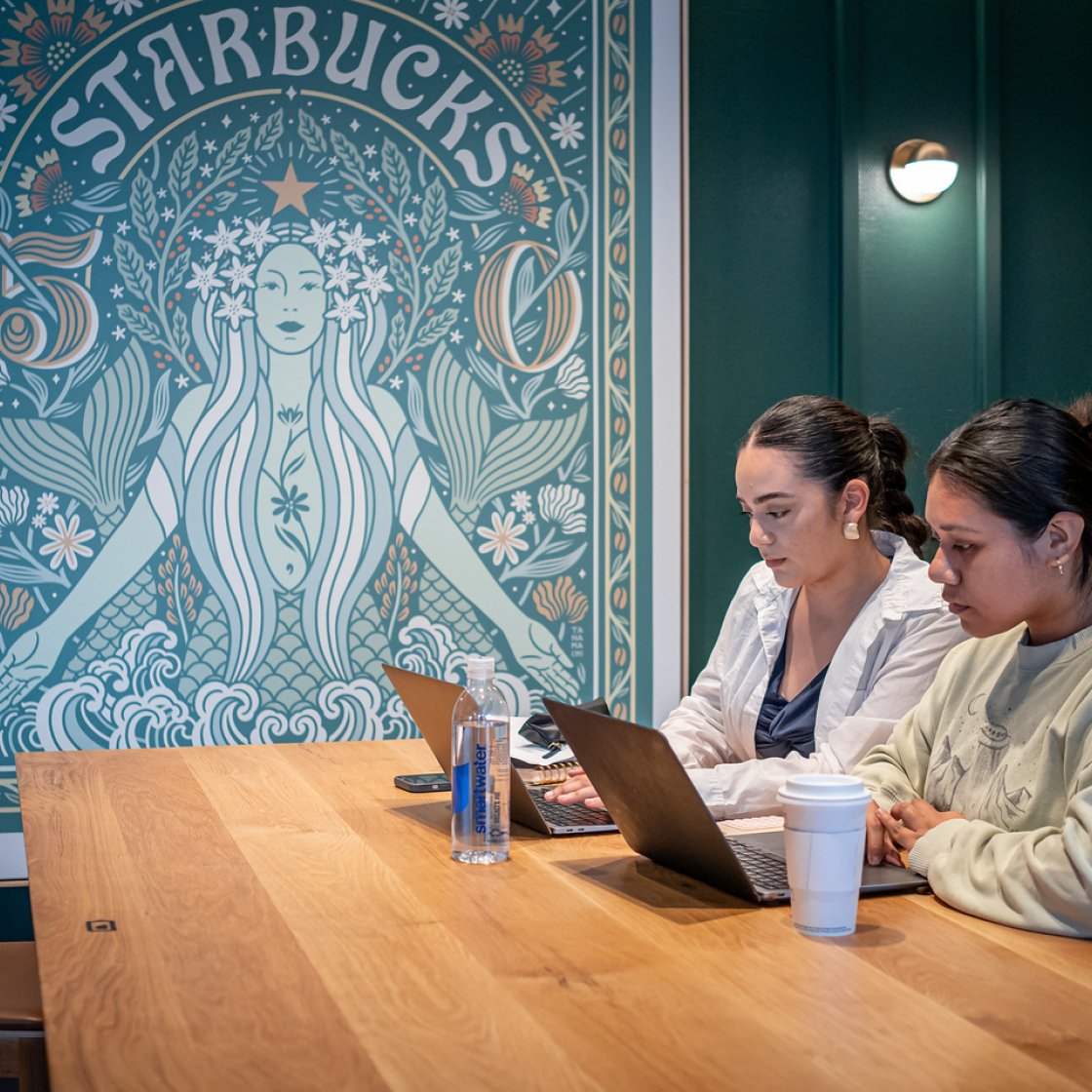 Two students sat inside a Starbucks on their laptops.