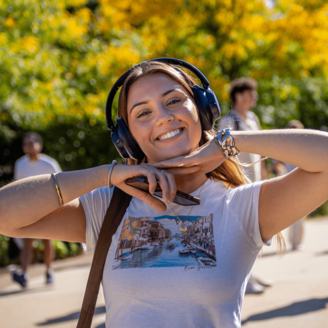Female student on campus smiling with headphones on with her hands under her face.