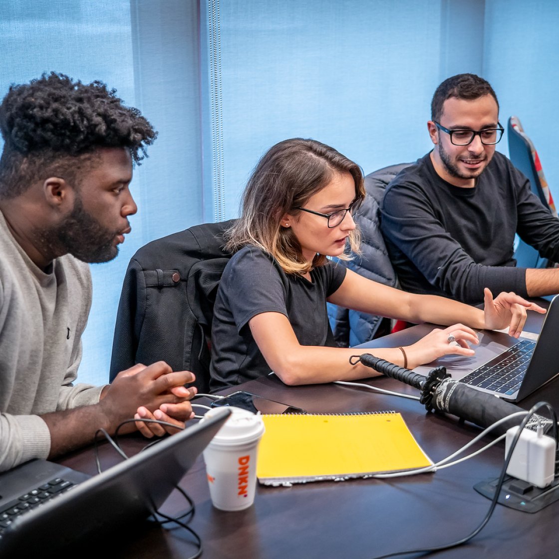 Three students are sitting down looking at a laptop having a discussion.