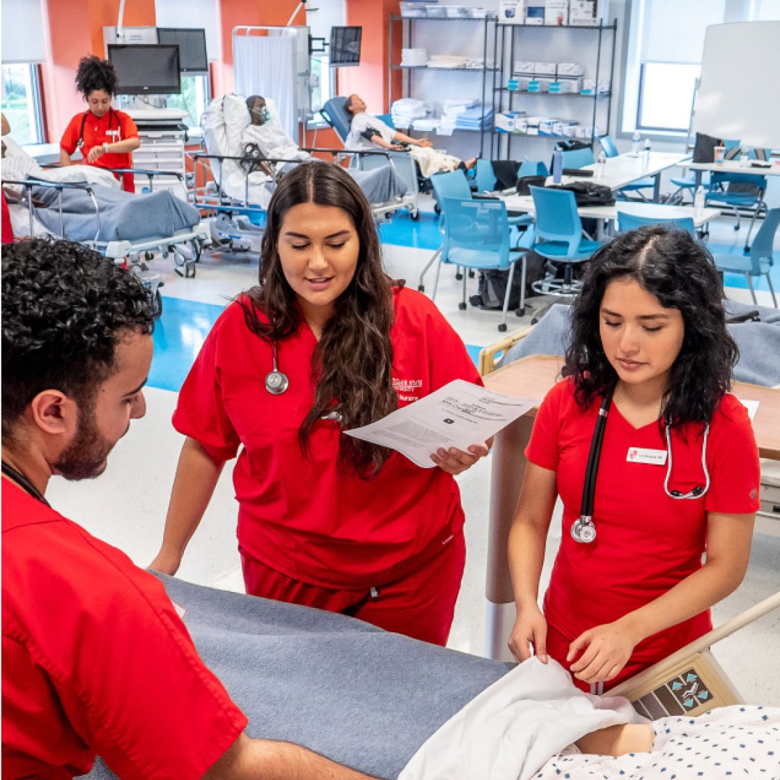 Three nursing students around bed with dummy
