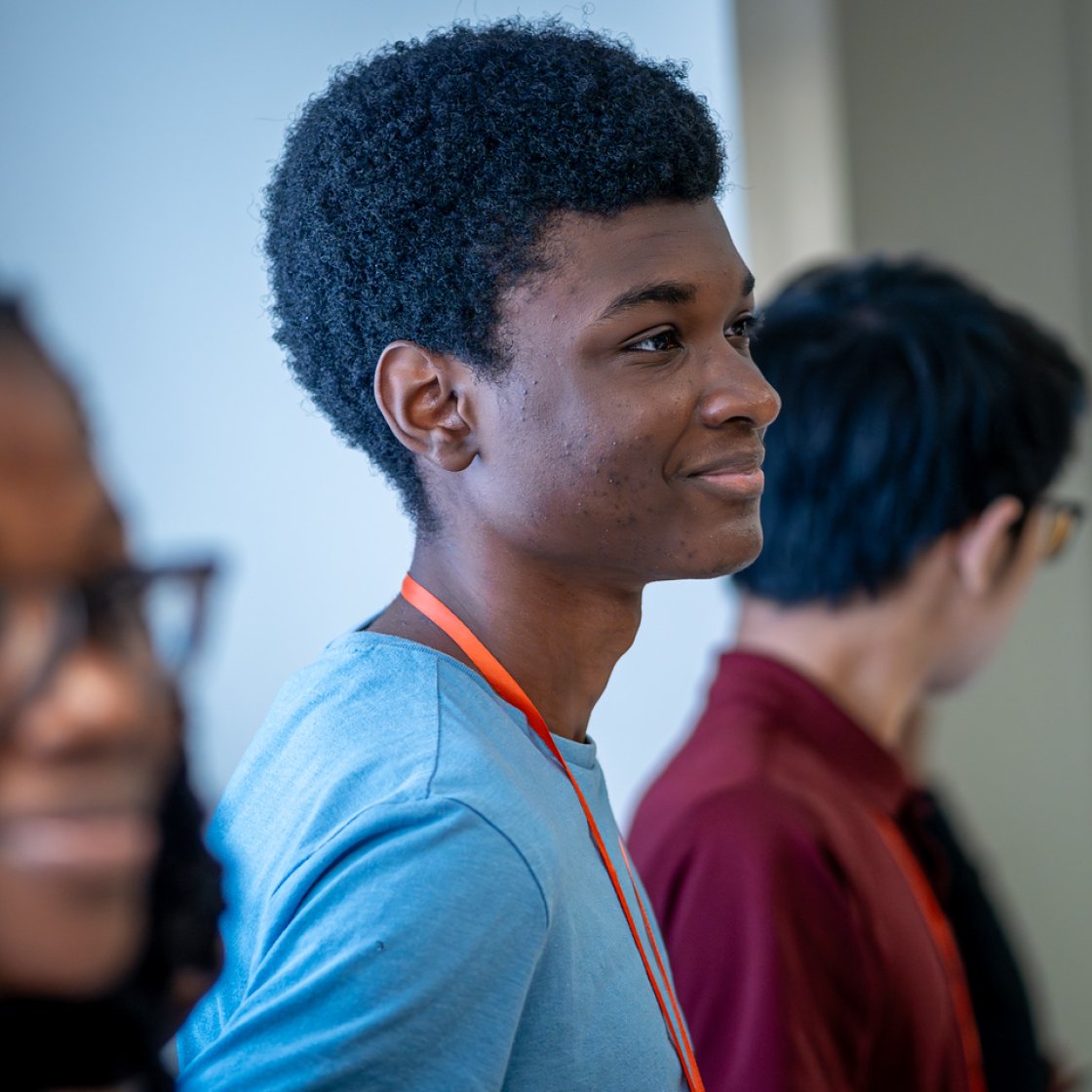 A student wearing a light blue T-shirt stands indoors in profile.