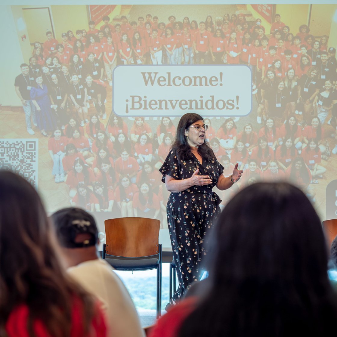 Woman on stage at HSCI orientation with the words Welcome behind her.