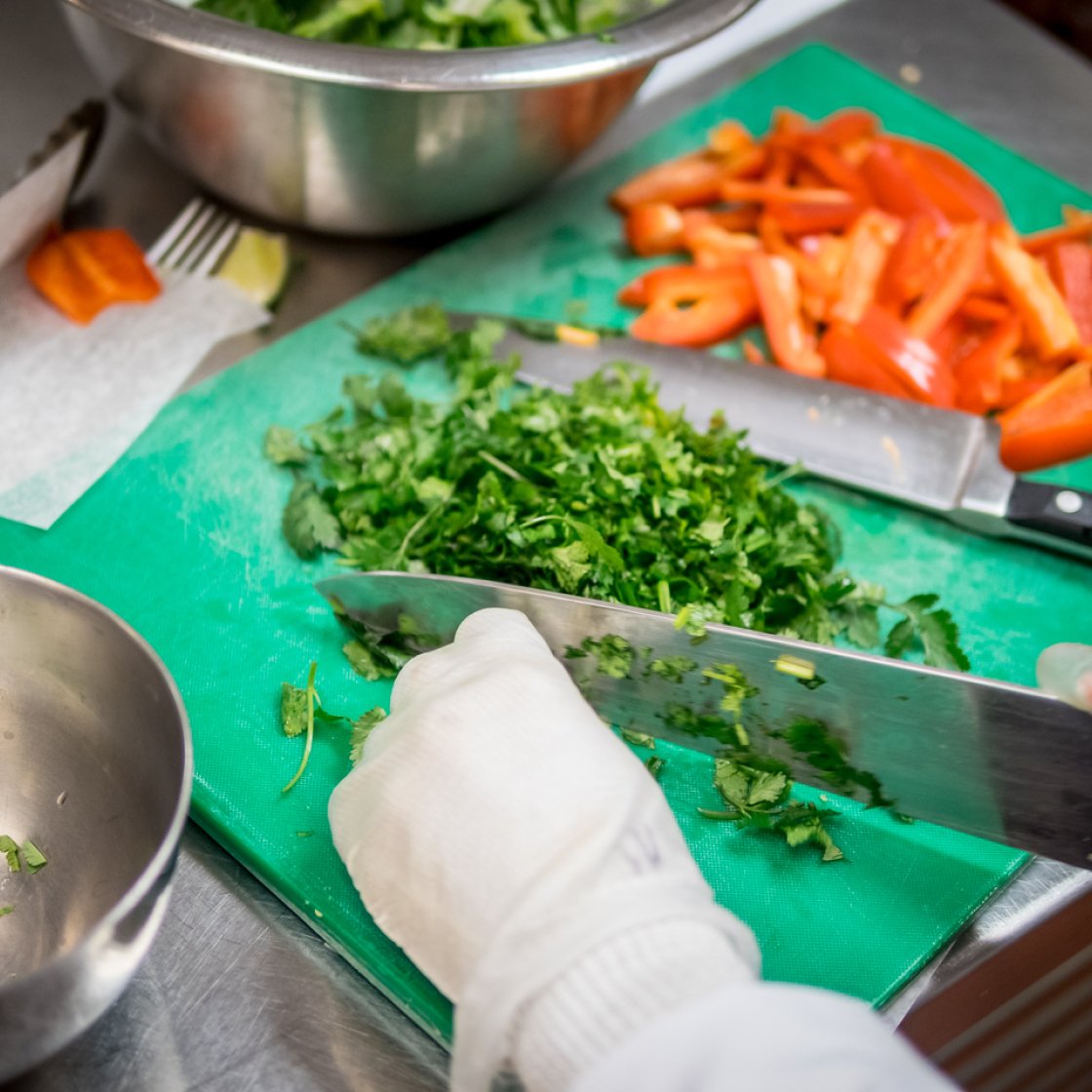 Someone is using a knife to cut cilantro on a green cutting board next to cut up peppers.