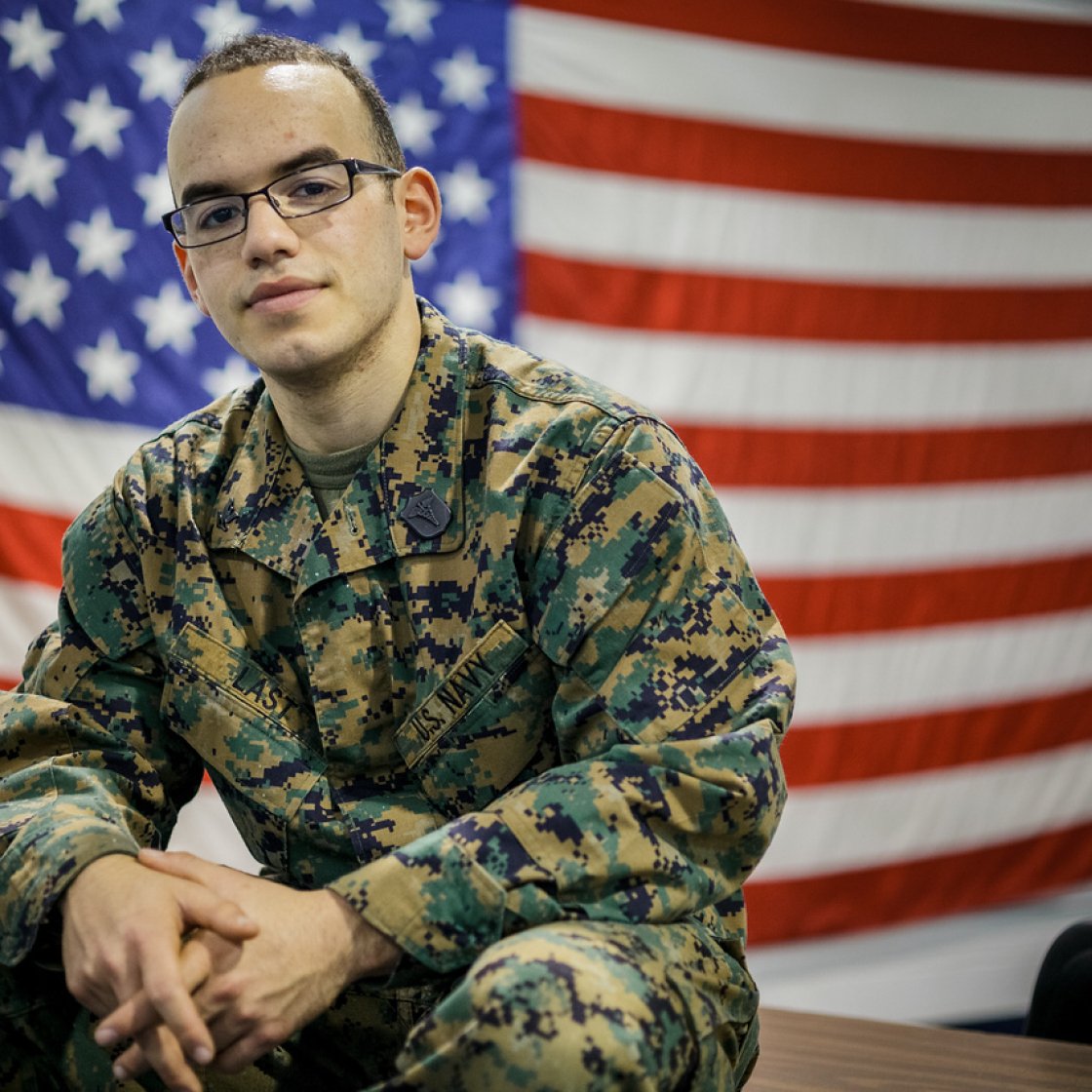 Man in military camo hear sitting down in front of a USA Flag.