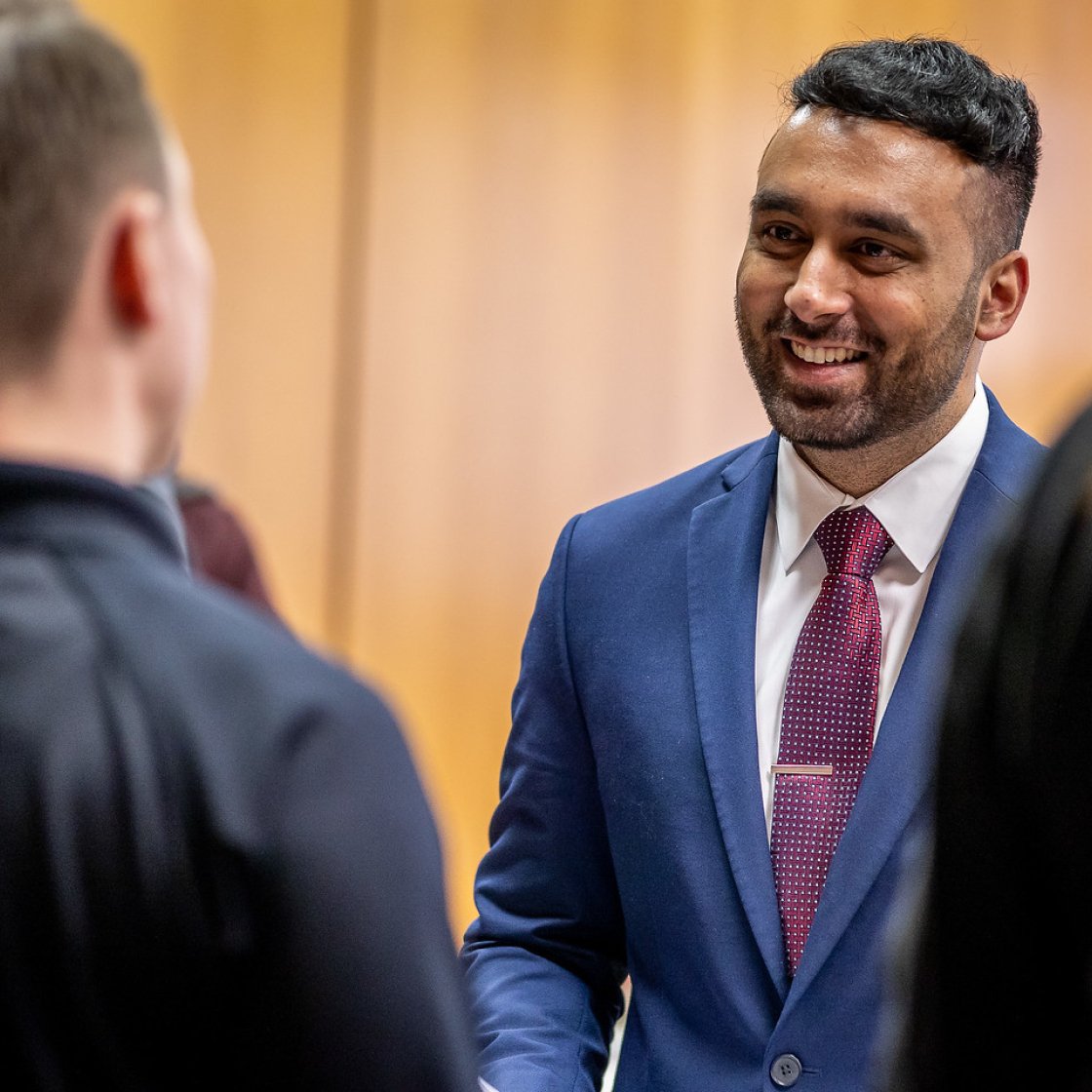 Man in a suit at a career fair speaking with another individual.