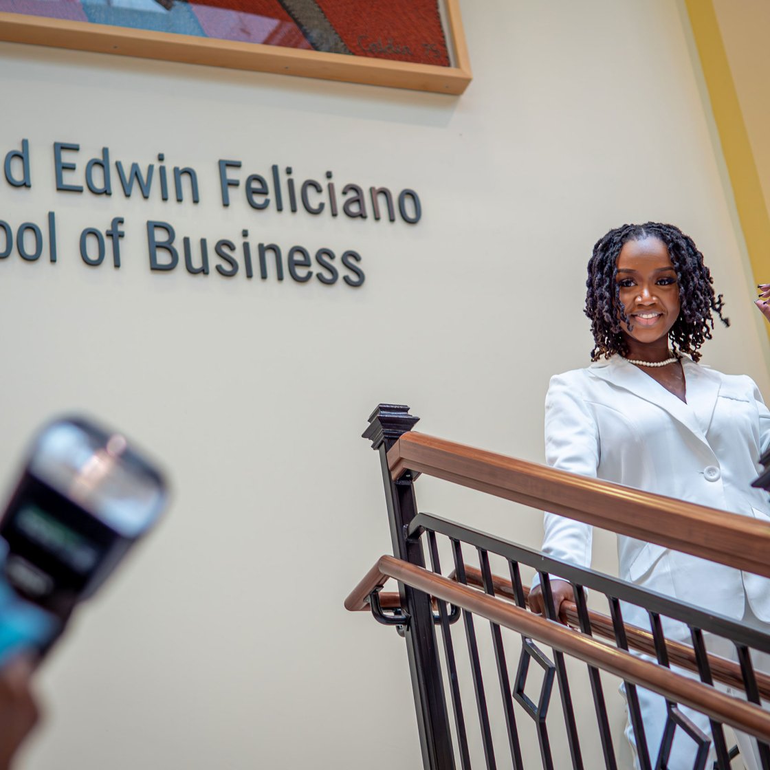 Student smiling at the camera as they stand in the Feliciano School of Business building.