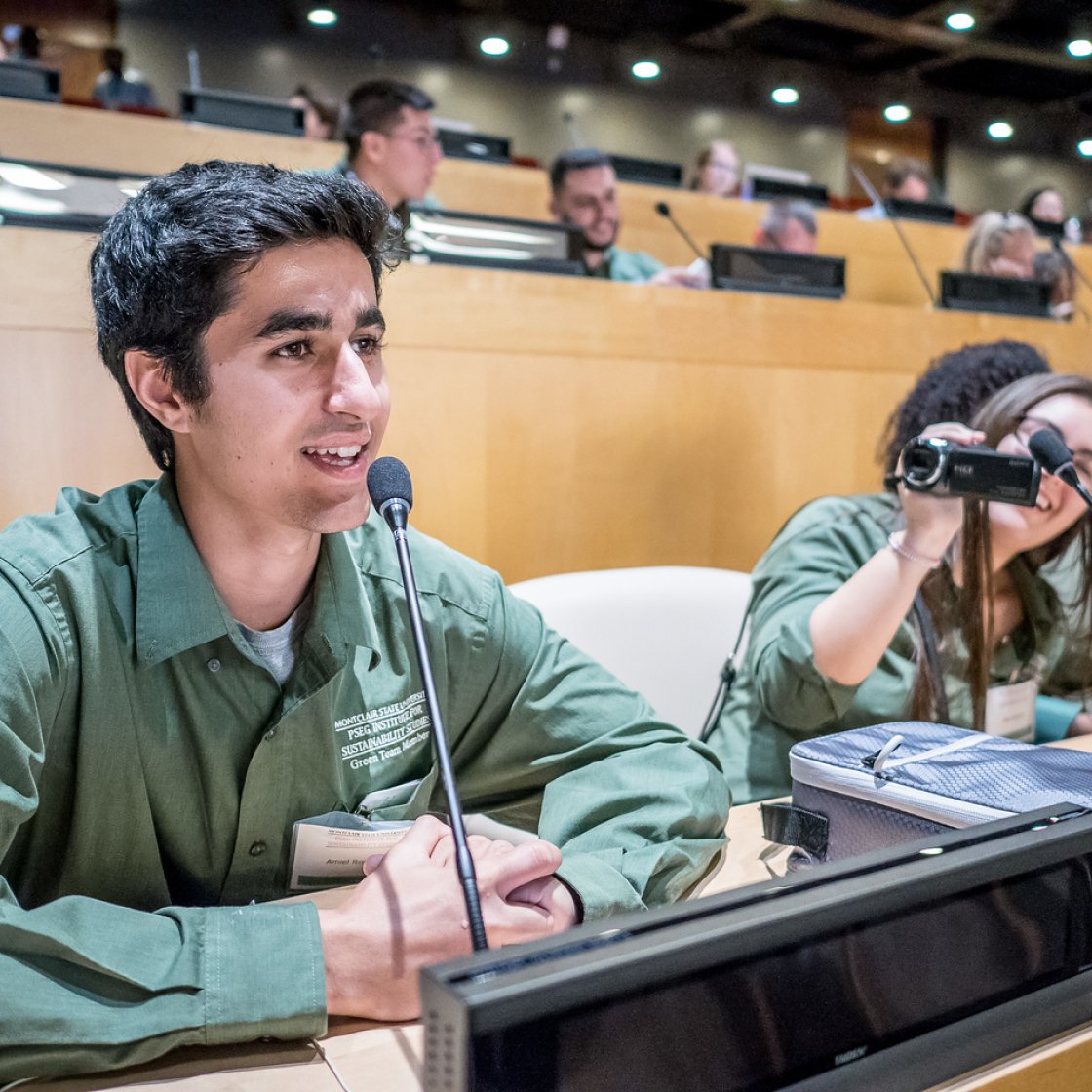 Male student speaking at UN, with a classmate recording with a video camera.