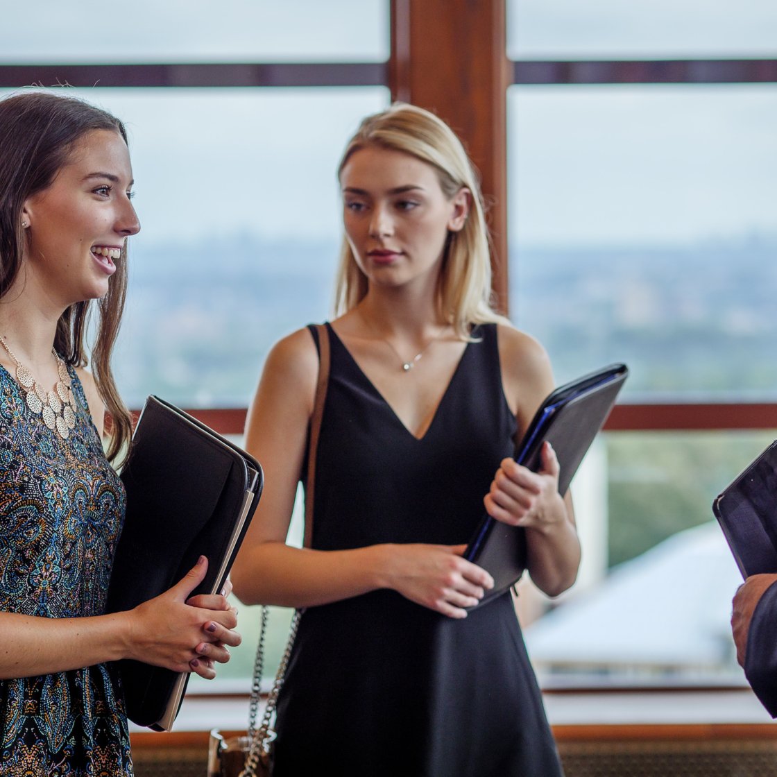 Two women are at a job fair with black notebooks in their hands.