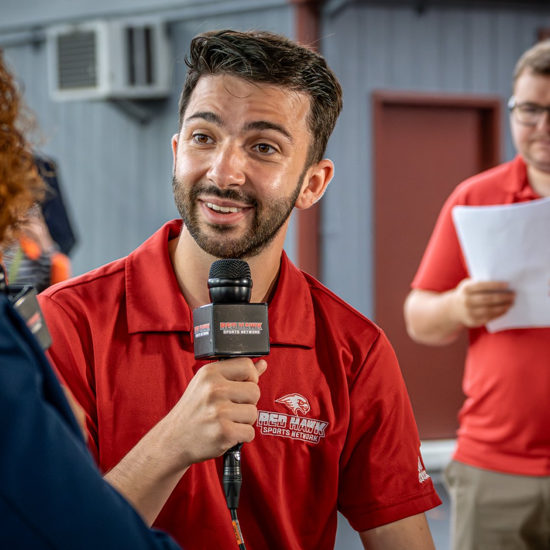 Man is holding a mic speaking with someone out of frame.