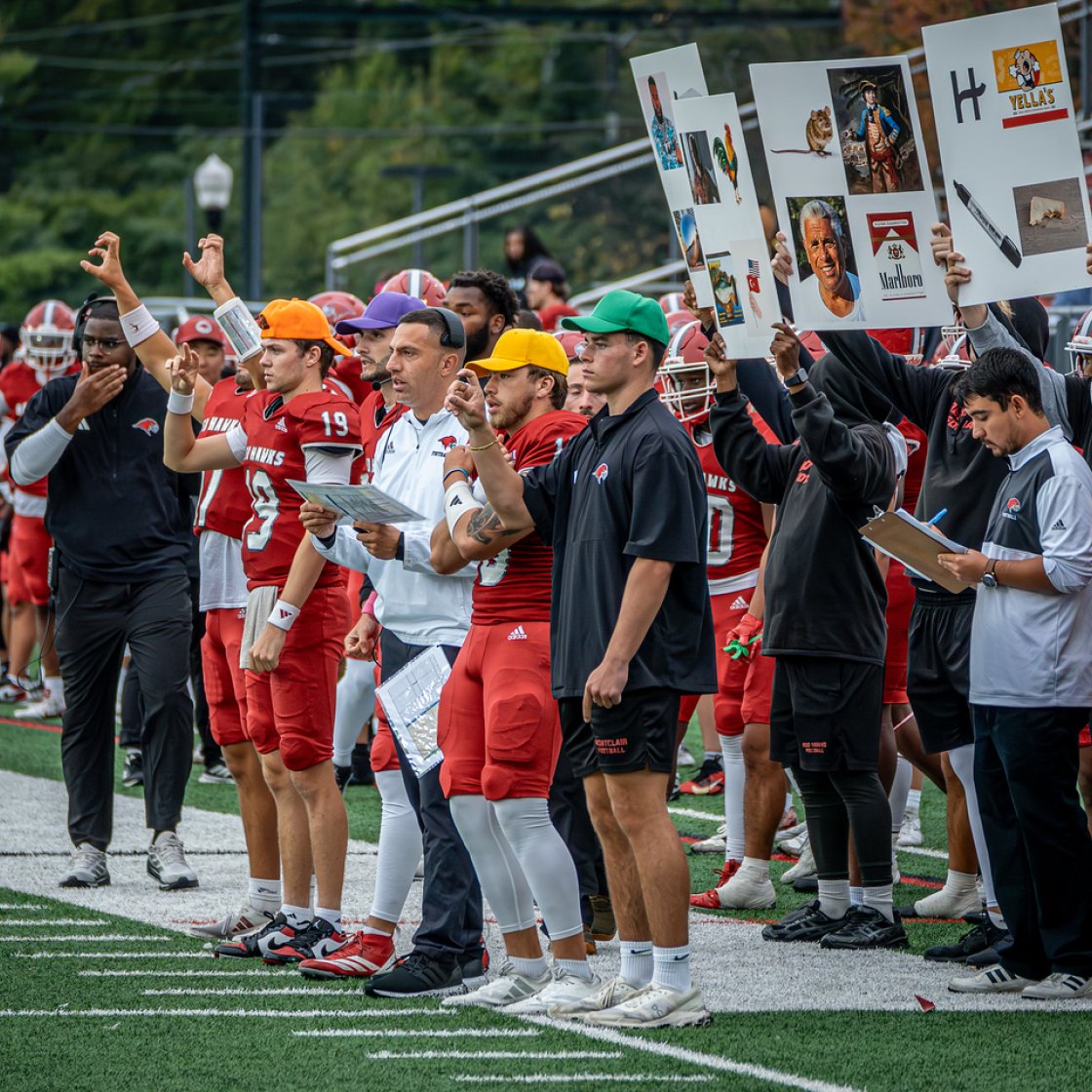 Sidelines of a football match, everyone attentive while some hold posters up.