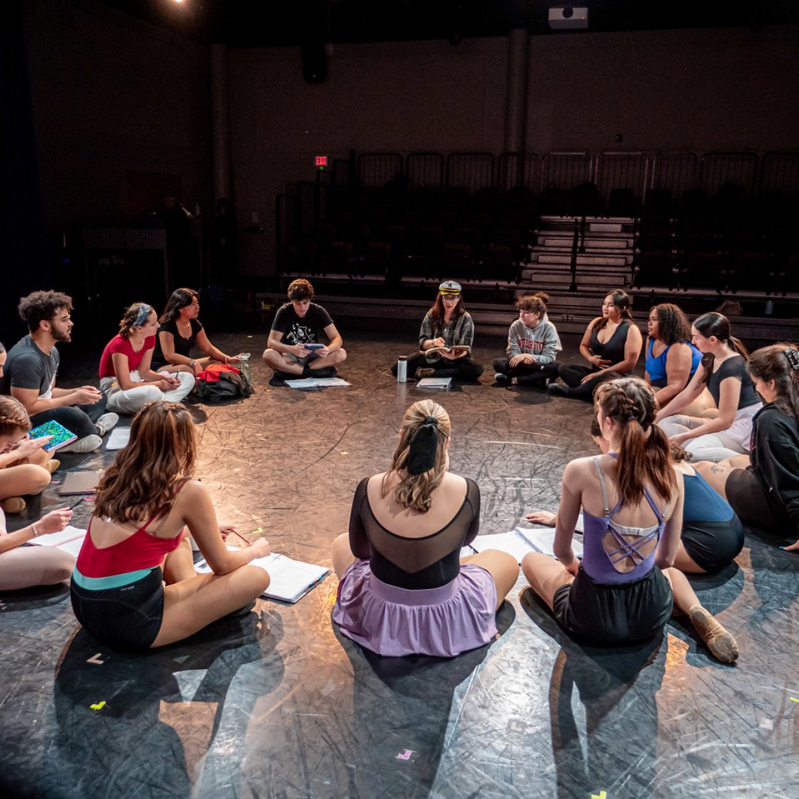 Group of students sat in a circle in dance outfits.