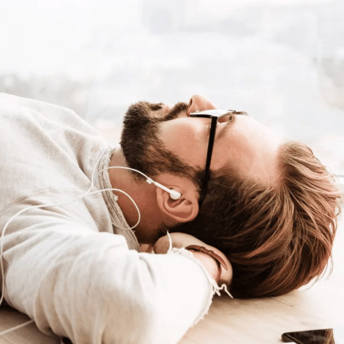 A man lies on his back listening to a podcast through earbuds.