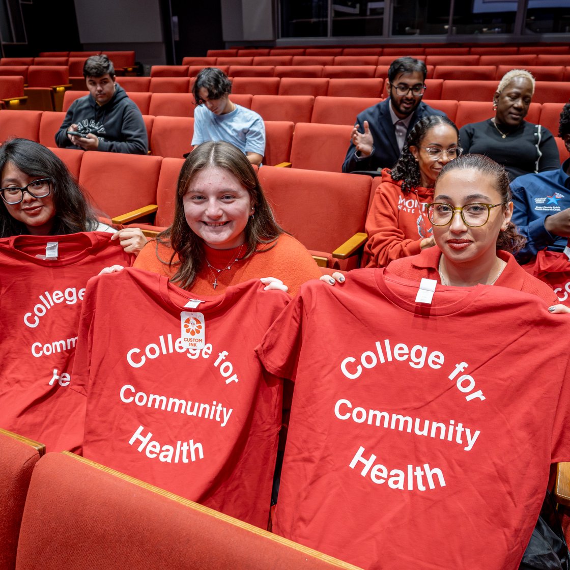 Three CHSS students are holding up red shirts with the words College for Community Health on the shirts.