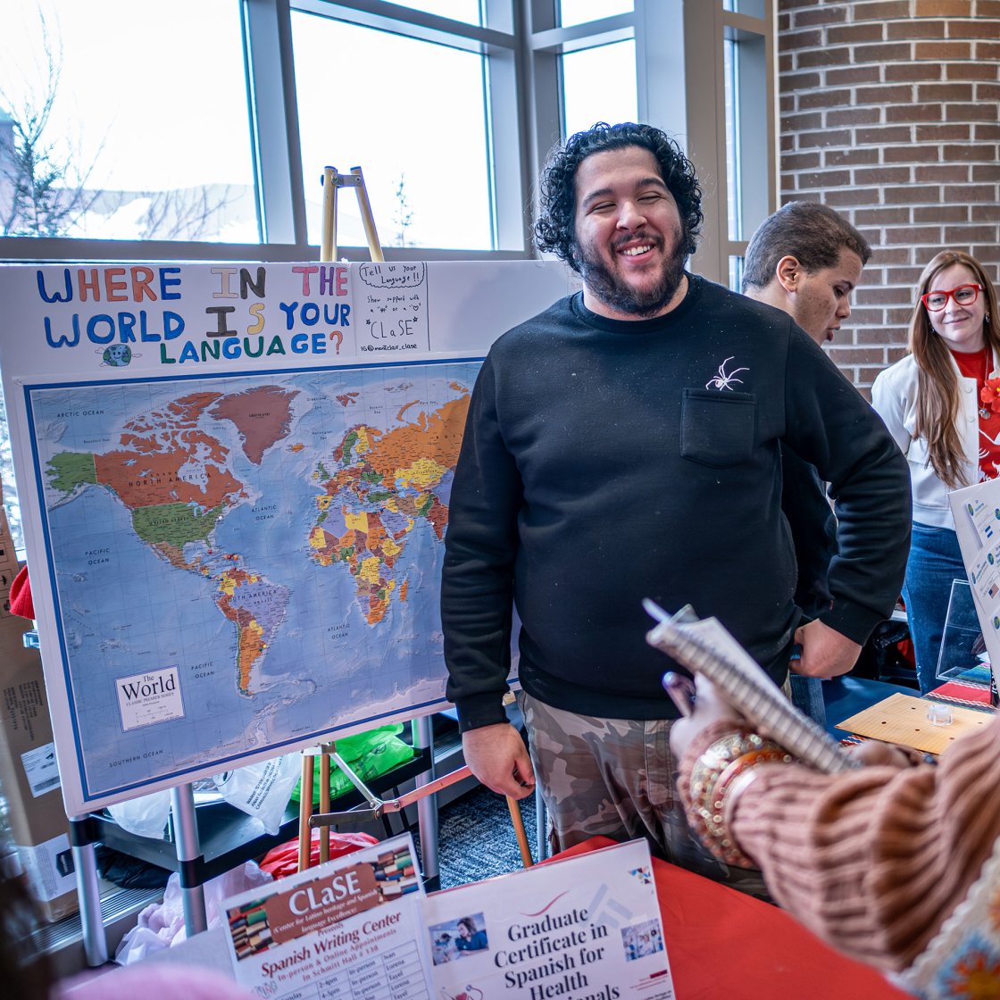 Two people talking at a language fair with presentation board labeled "where in the world is your language"