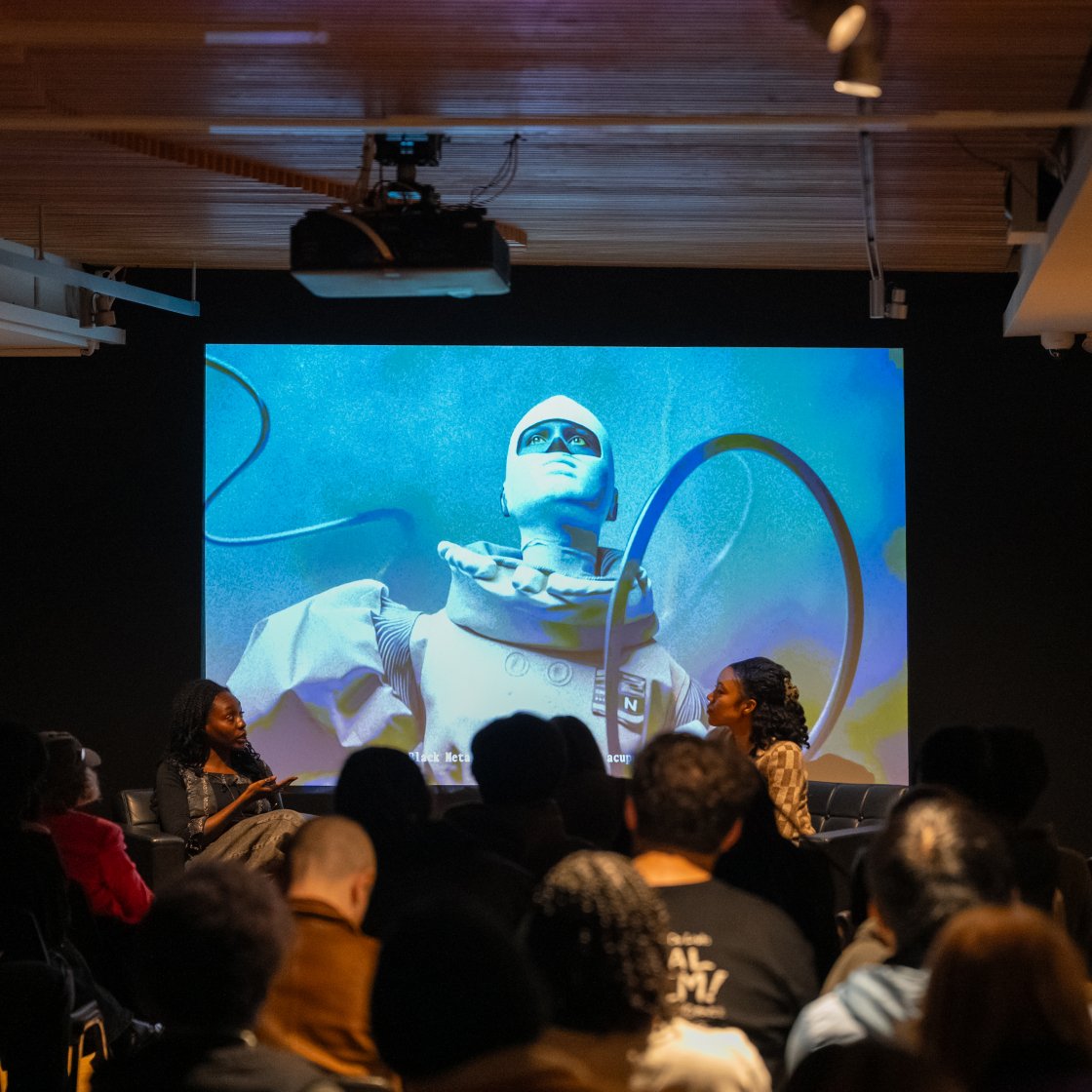 Students listening to presenters in front of a projector.