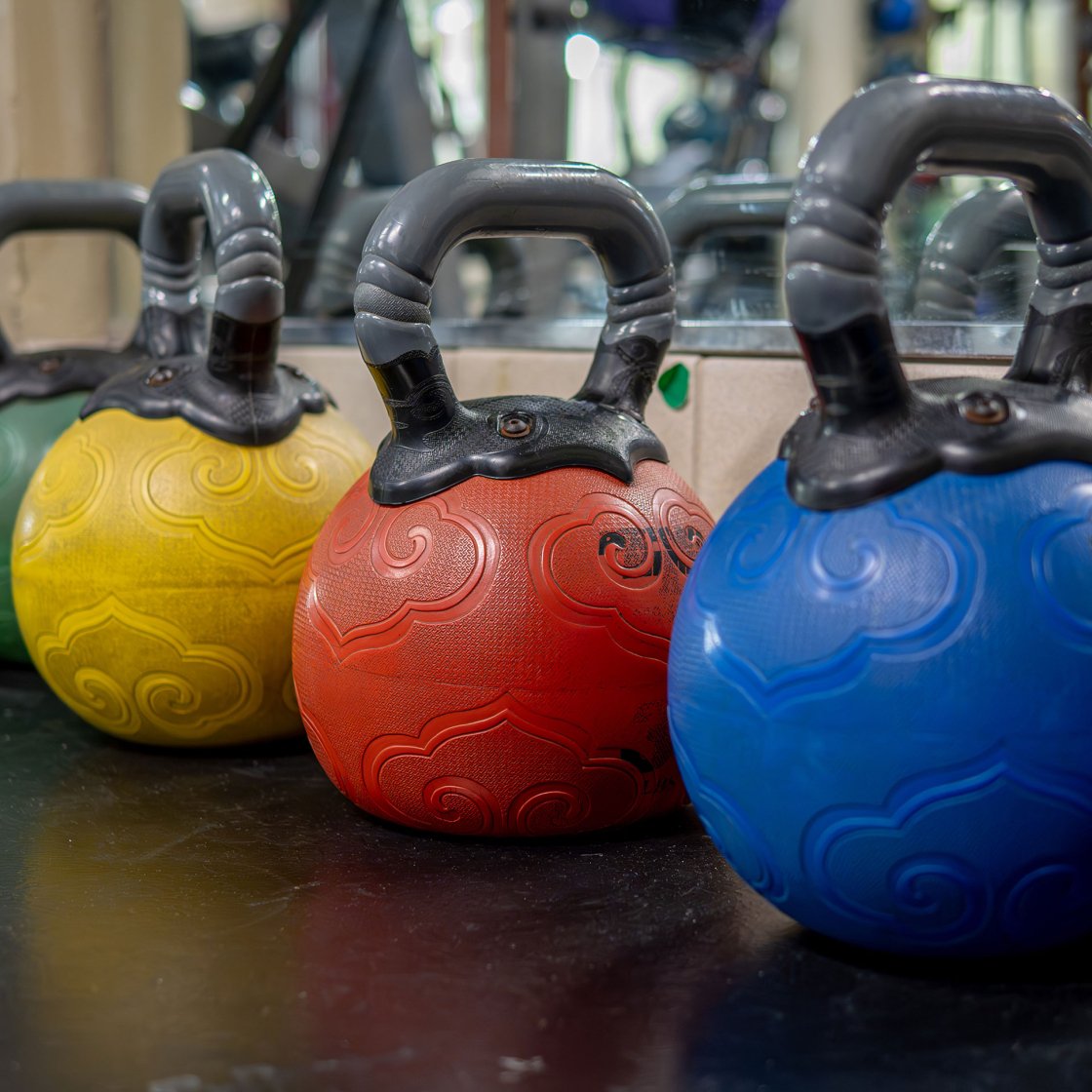 Green, yellow, red, and blue ball weights lined up on a gym floor.
