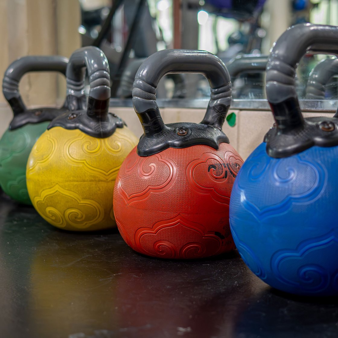Green, yellow, red, and blue ball weights lined up on a gym floor.