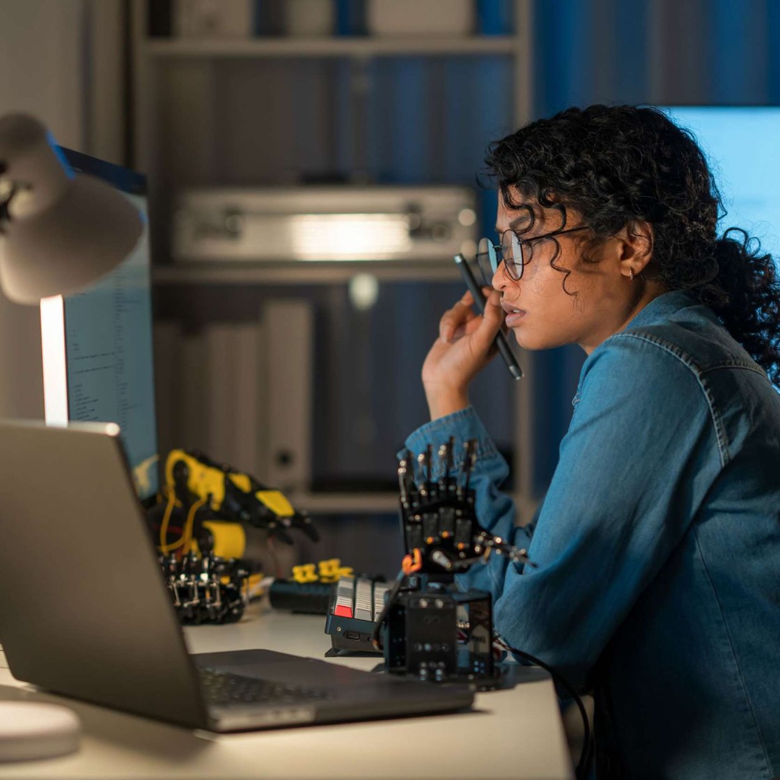 Female graduate student with robotics parts and open laptop.