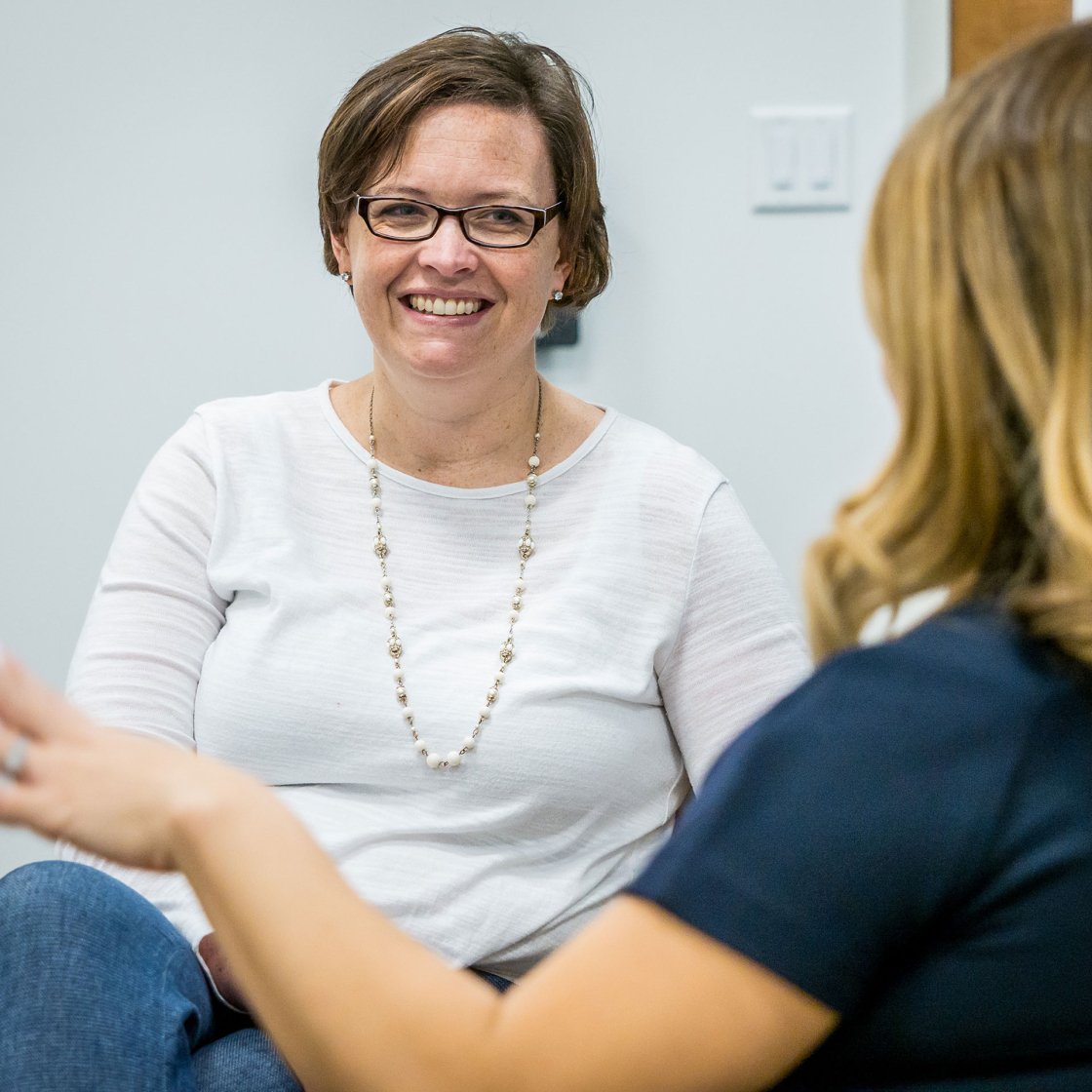 Two people speaking to one another. One is smiling as the other moves their hand.
