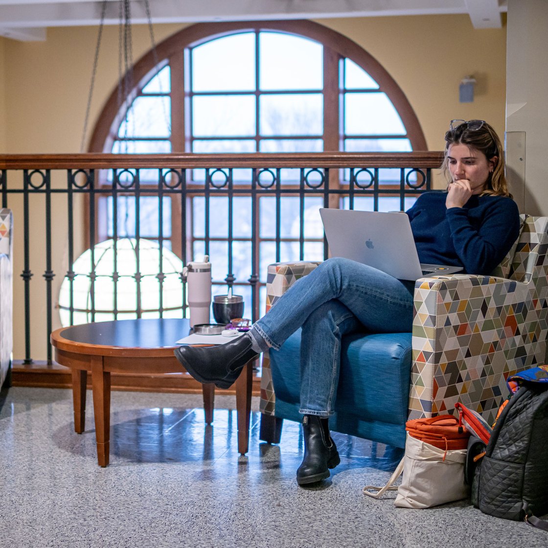 Student studying on one of the sofas in University hall. They are using a laptop.