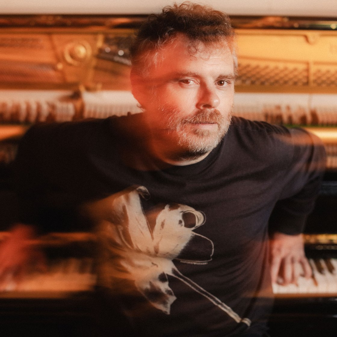 Gabriel Kahane sitting with back towards piano and hands on keys
