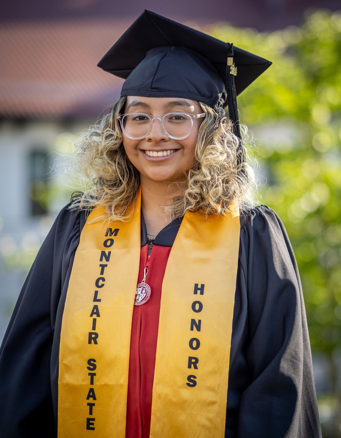 Mariana Luna-Martinez, in cap and gown and a yellow stole that says Montclair State Honors.