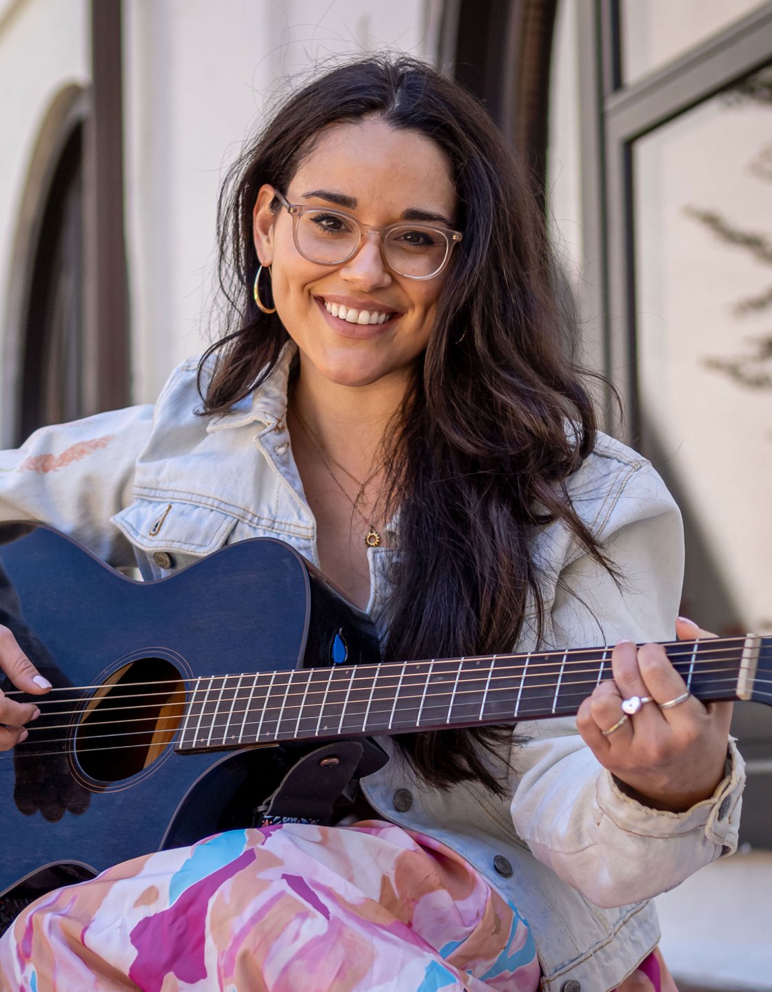 Alyssa Muñiz smiling at the camera and playing the guitar.