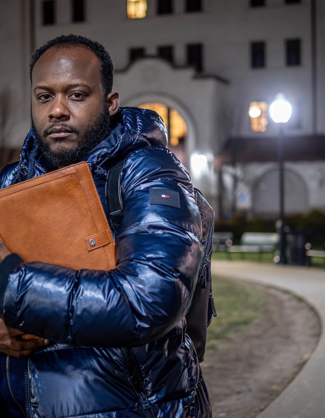 Horatio Wauchope stands in front of a college building in the evening, wearing a winter parka and carrying a portfolio. 