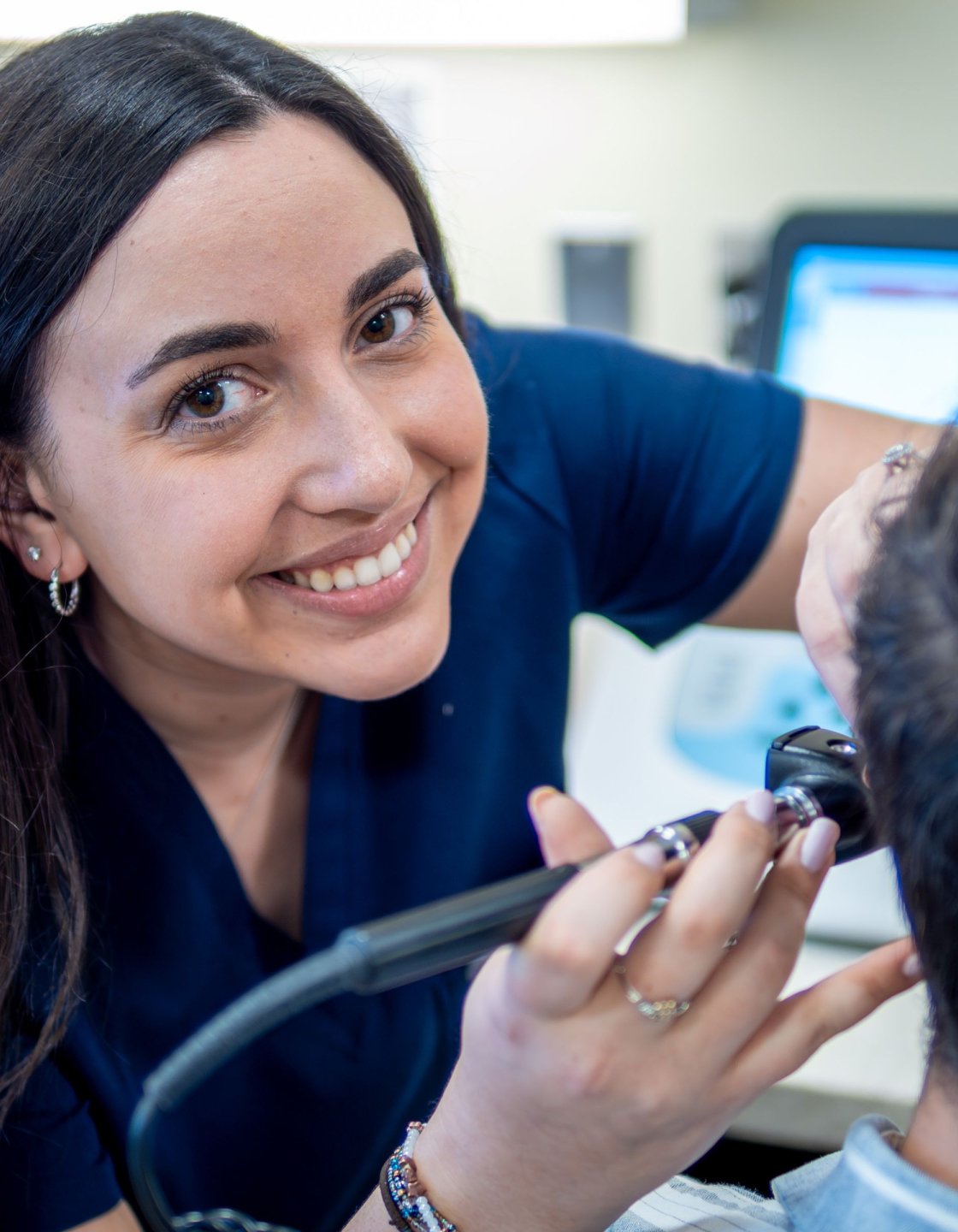 Nicole Genser checking a patient's ear and smiling at the camera.