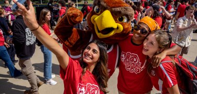 A group of students wrangles Rocky the Red Hawk for a selfie at the Red Hawk Day street fair