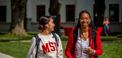 Two female students are walking through campus, conversing.