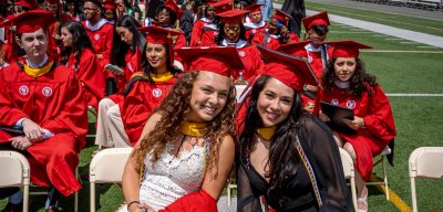 Two females at CHSS convocation smiling with a red grad cap.