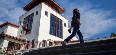 A person walks up the steps outside the Alexander Kasser Theater at Montclair State University under a bright blue sky.