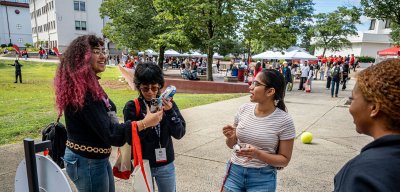 Three students talking to eachother in front of a booth. Another student is working the booth.
