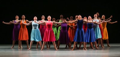 Performers on stages looking up with different colored dressed and their arms spread out.