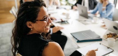 Person with long hair and glasses smiling at a conference table